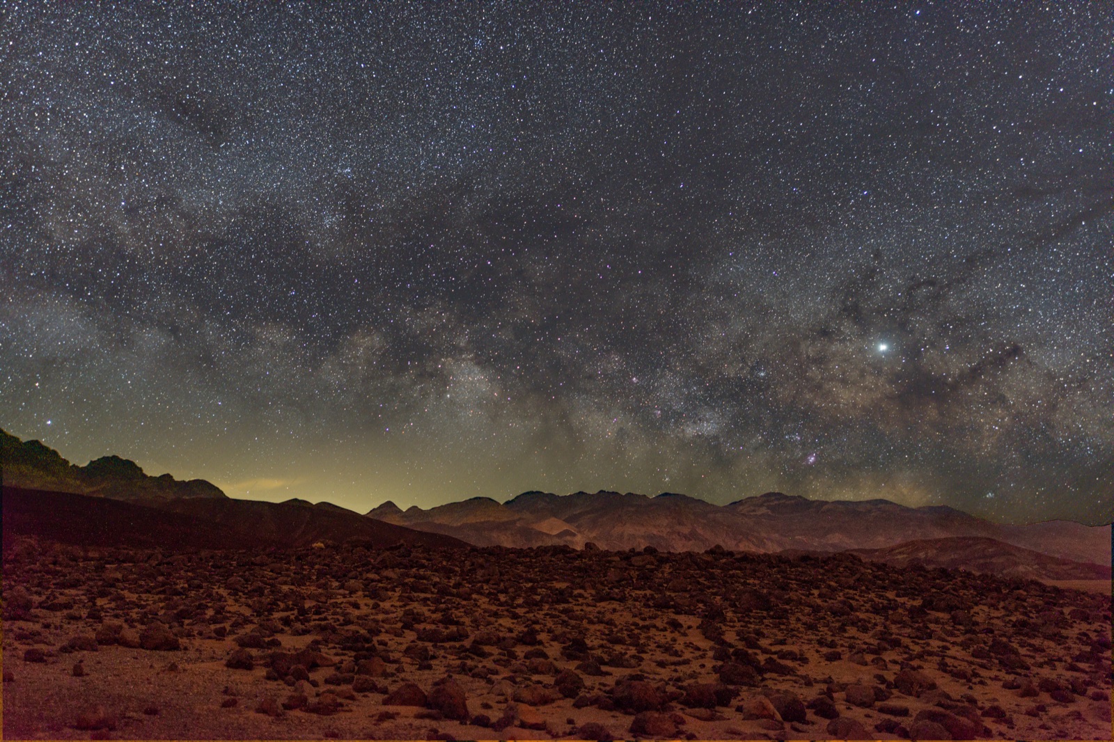 The Milky Way arching over a rocky desert plain and distant ranges in Death Valley National Park.